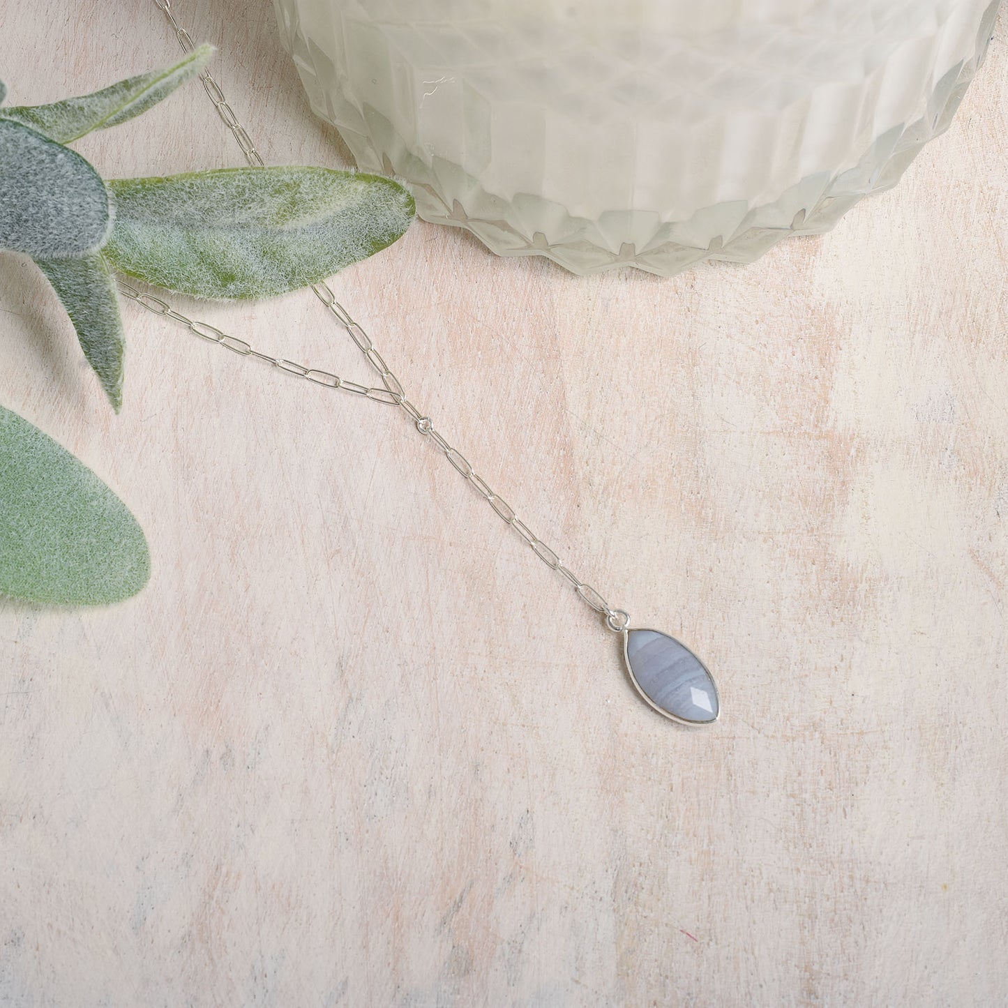 Necklace with a marquise-shaped pendant on a light wooden surface with a plant leaf.