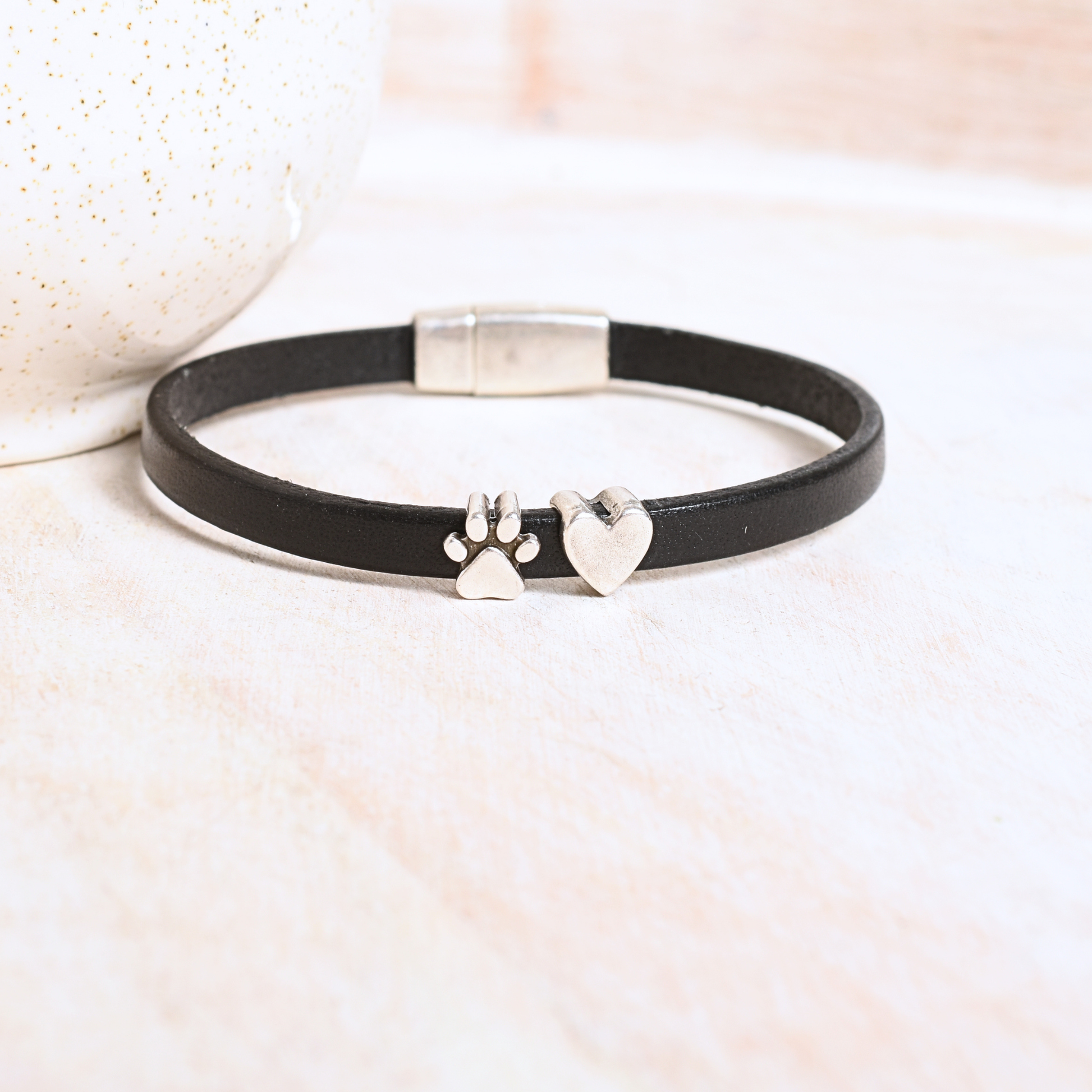 Black leather bracelet with silver paw print and heart charms on a light background