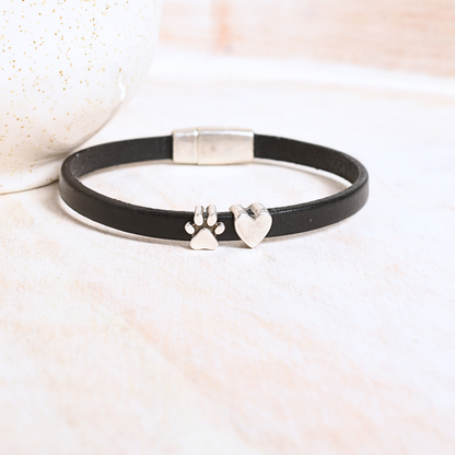 Black leather bracelet with silver paw print and heart charms on a light background