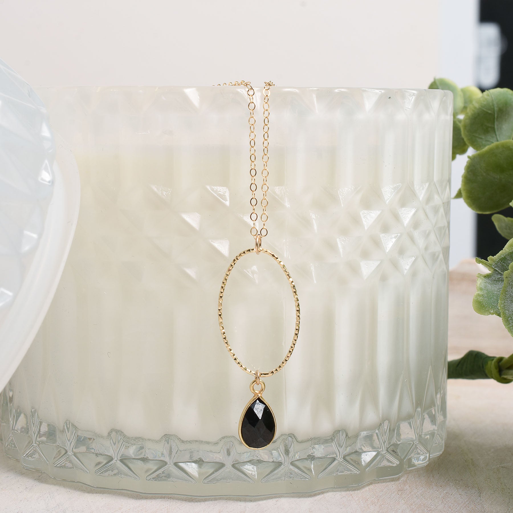 Gold necklace with a black spinal teardrop pendant on a textured white candle