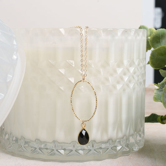 Gold necklace with a black spinal teardrop pendant on a textured white candle