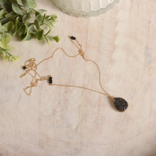 Necklace with a teardrop-shaped pendant on a light wooden surface with greenery.