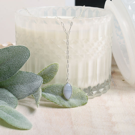 Silver necklace with a marquise-shaped agate pendant on a white candle and green leaves