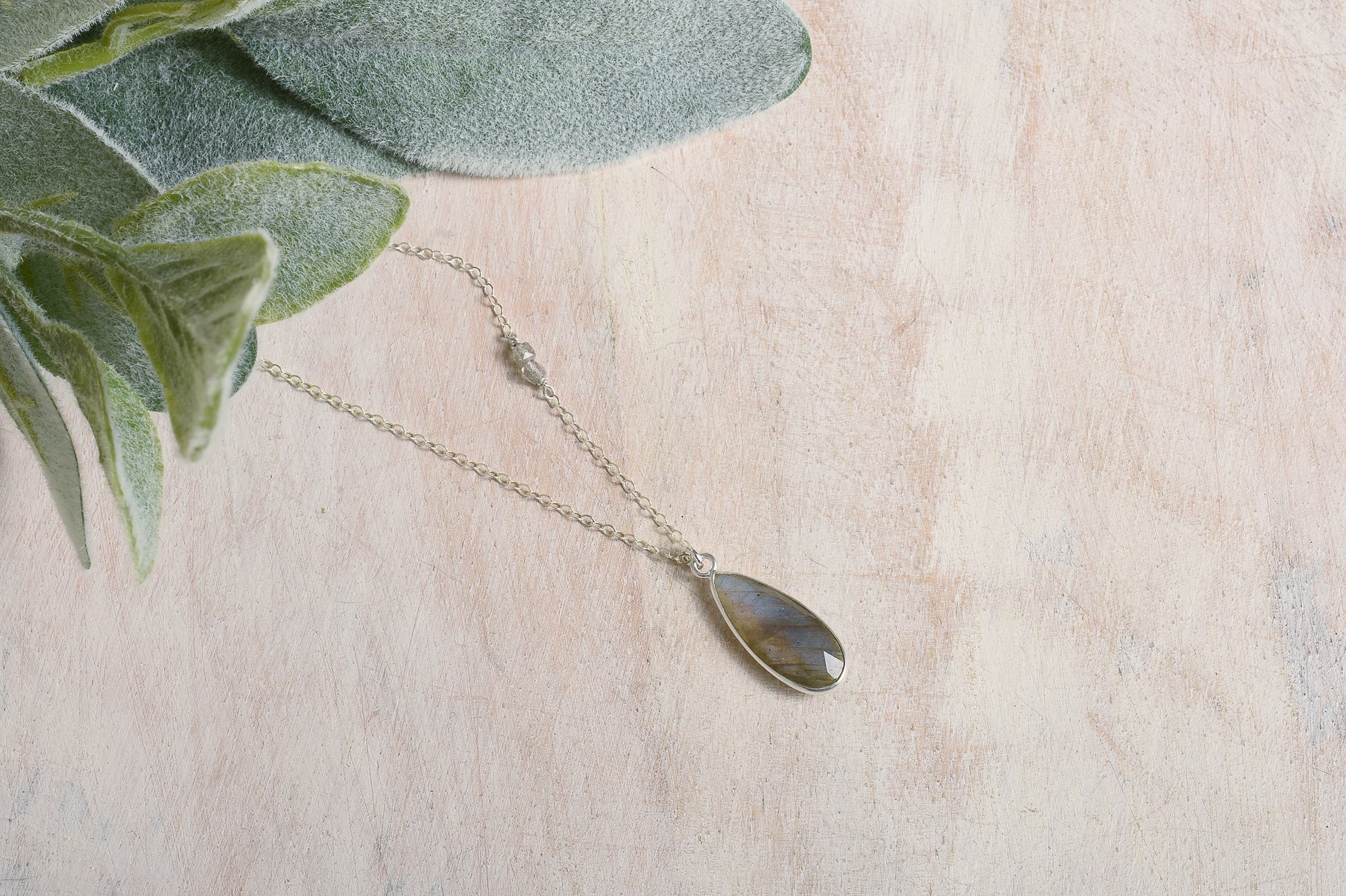 Necklace with a teardrop labradorite pendant on a light background with green leaves.