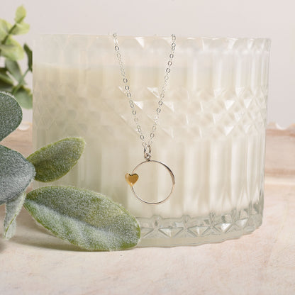 Necklace with a heart pendant on a textured glass surface with green leaves in the background