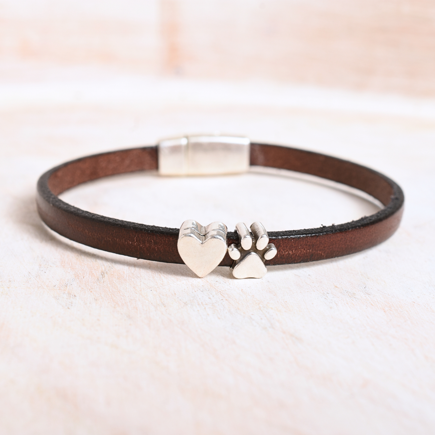 Brown leather bracelet with silver heart and paw charm on a light background