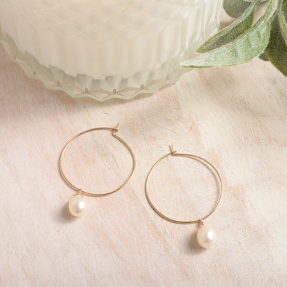 Gold hoop earrings with pearls on a beige surface 