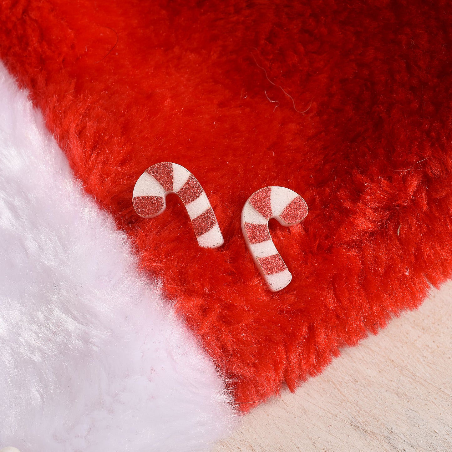 Glittery acrylic earrings in a candy cane shape on a red and white background.