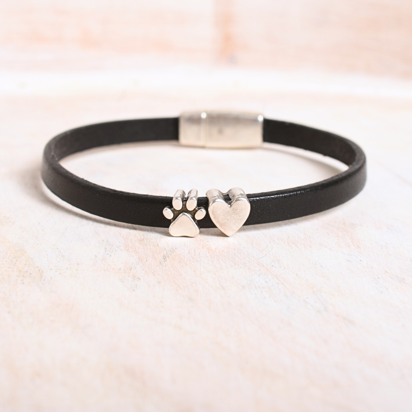 Black leather bracelet with paw and heart charms on a light background