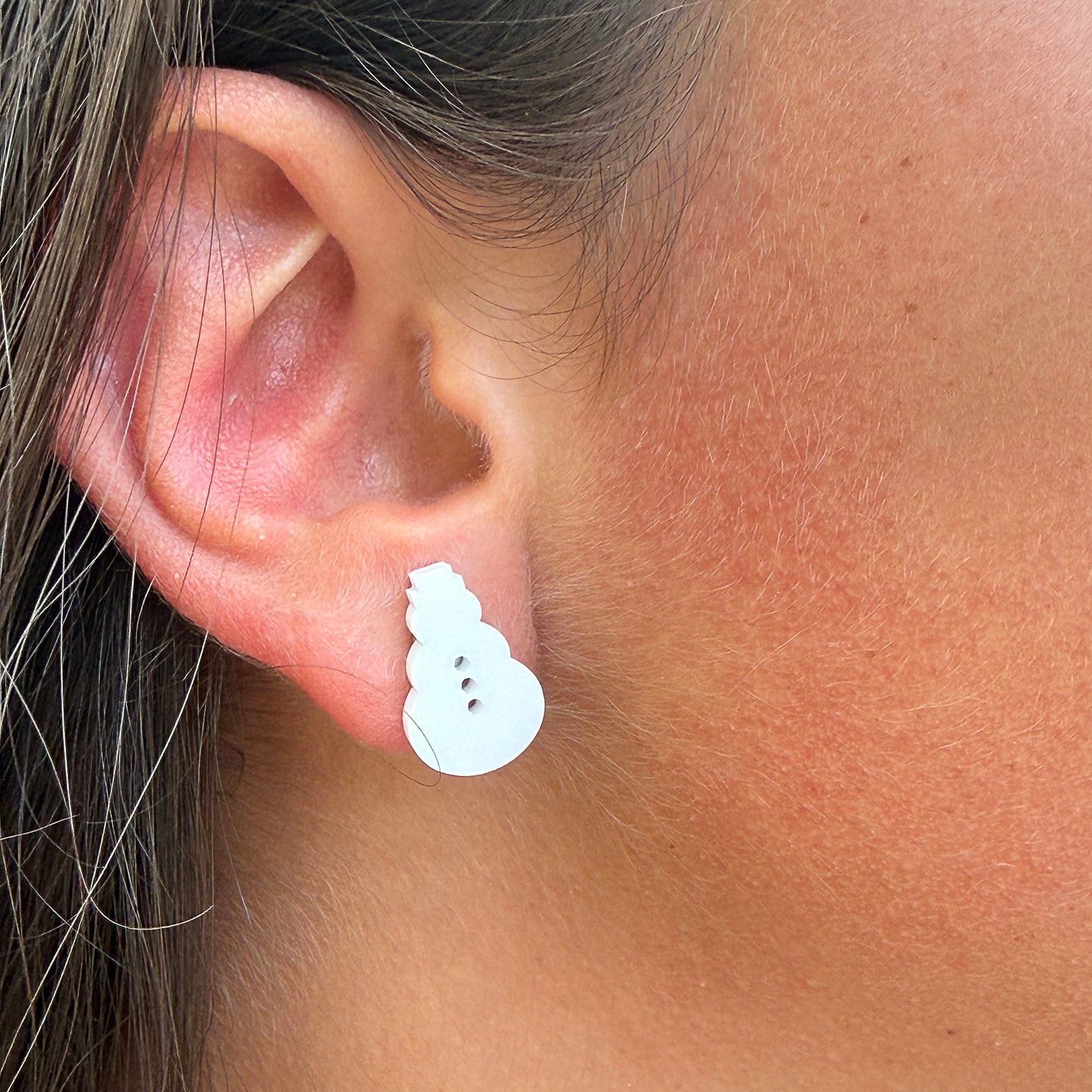 A close-up of a person's ear wearing a small white snowman stud earring.
