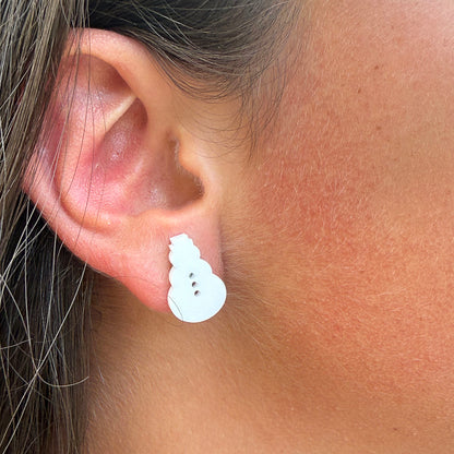 A close-up of a person's ear wearing a small white snowman stud earring.