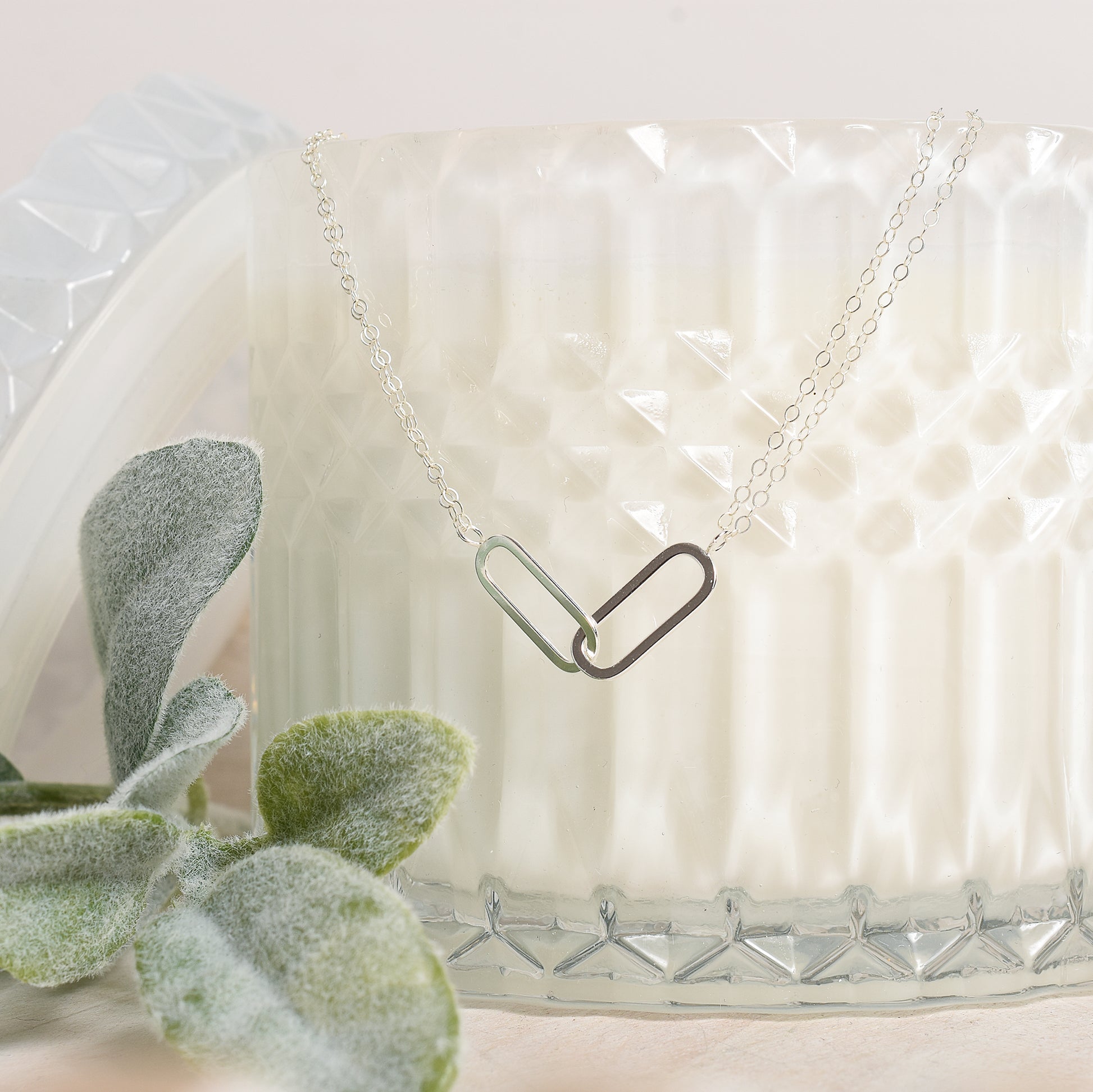 Necklace with a unique pendant design on a textured white surface with a plant.