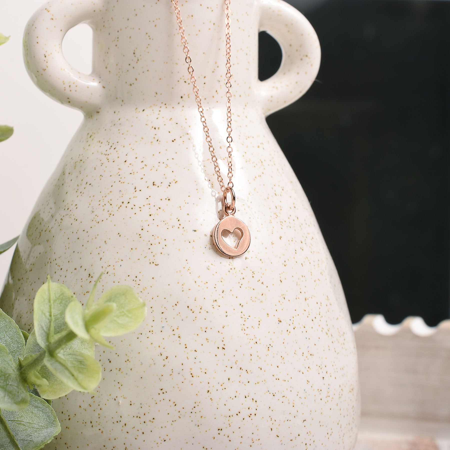 Rose gold necklace with a heart pendant on a white speckled vase.