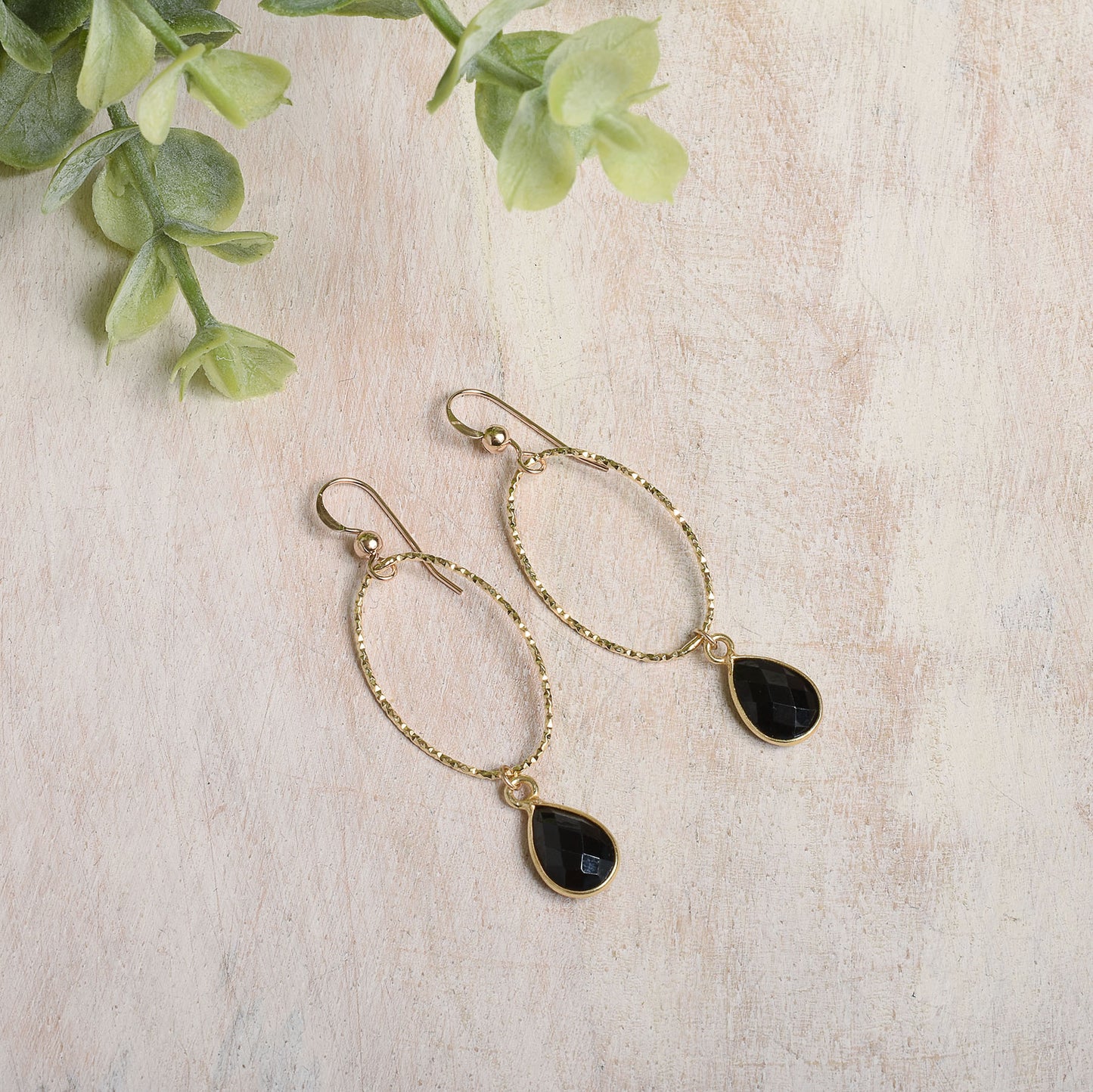 Gold-filled earrings with black spinel teardrop stones on a light background
