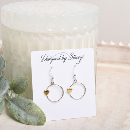 Pair of earrings on a card labeled 'Designed by Stacey' with a candle and plant in the background.