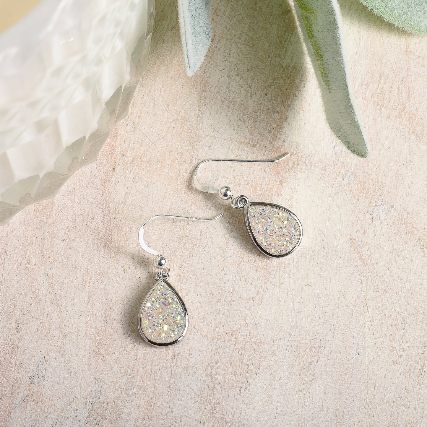 Teardrop-shaped earrings with glittery finish on a textured beige surface.