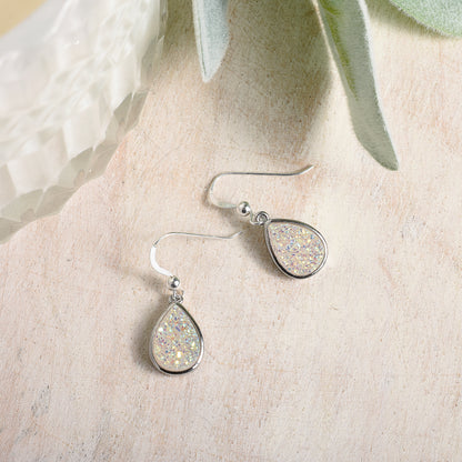 Teardrop-shaped earrings with glittery finish on a textured beige surface.