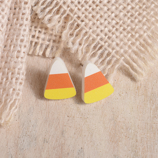 Candy corn shaped stud earrings with white, orange, and yellow stripes, displayed on a light wood surface with a burlap fabric backdrop.