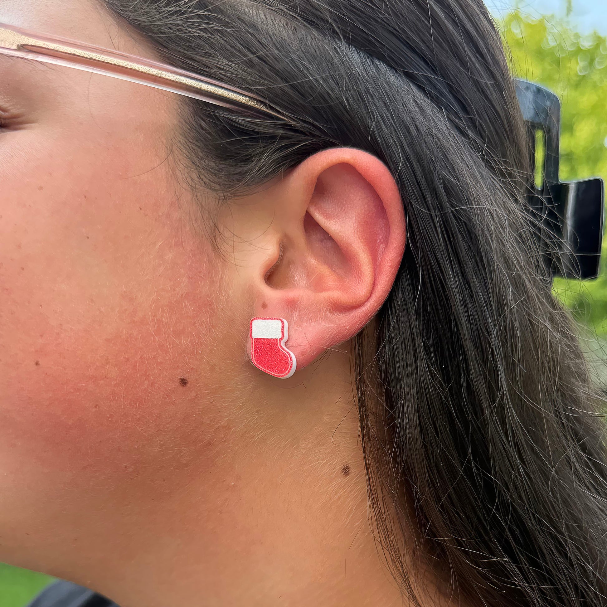 A close-up side profile of a person wearing a small red and white Christmas stocking stud earring.