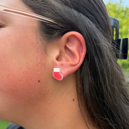 A close-up side profile of a person wearing a small red and white Christmas stocking stud earring.
