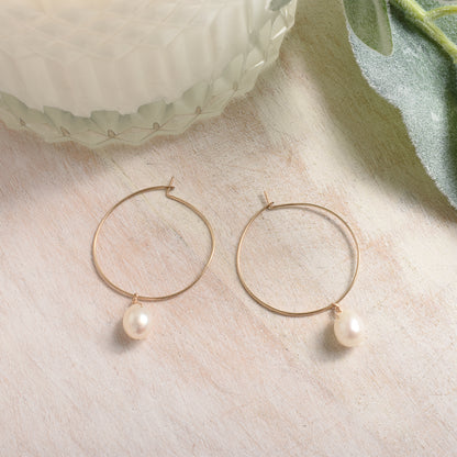 Gold hoop earrings with pearls on a light surface