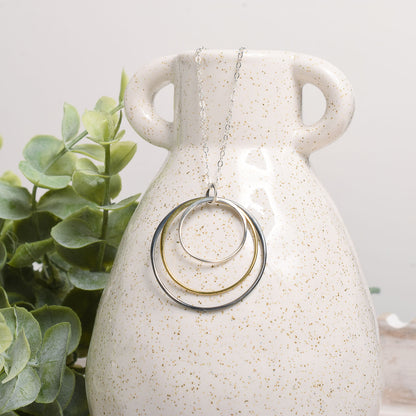 Necklace with circular pendants on a white speckled vase with greenery in the background