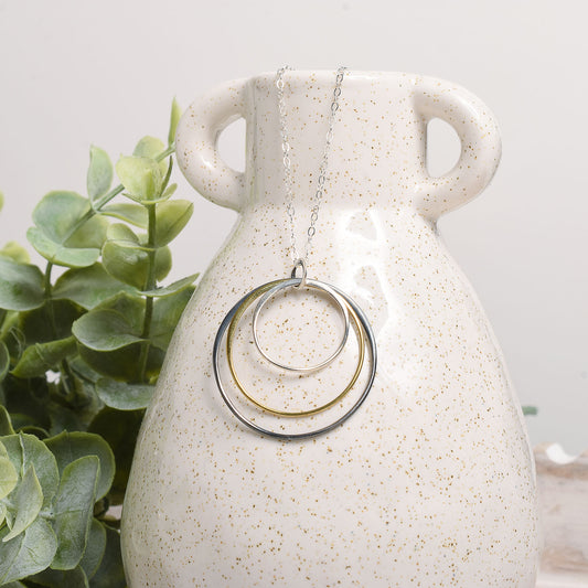 Necklace with circular pendants on a white speckled vase with greenery in the background