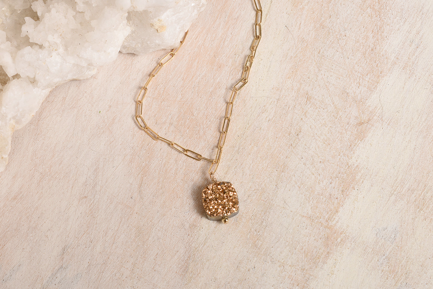 Gold necklace with a textured pendant on a light wood surface