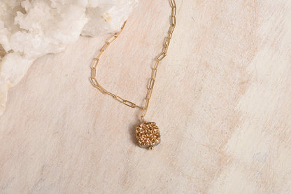Gold necklace with a textured pendant on a light wood surface
