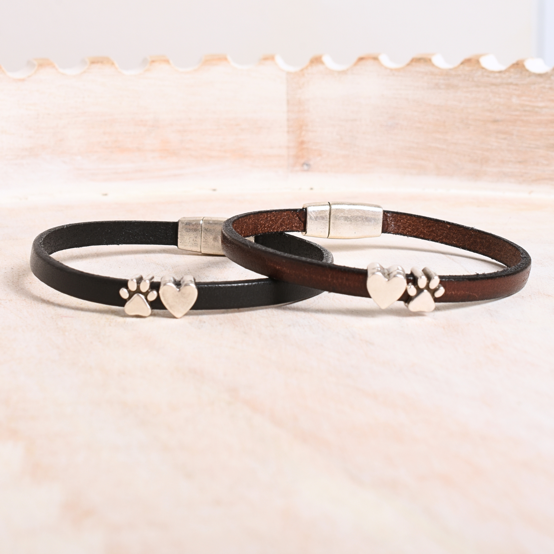Two leather bracelets with metal clasps and paw print designs on a light background