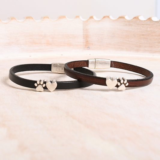 Two leather bracelets with metal clasps and paw print designs on a light background