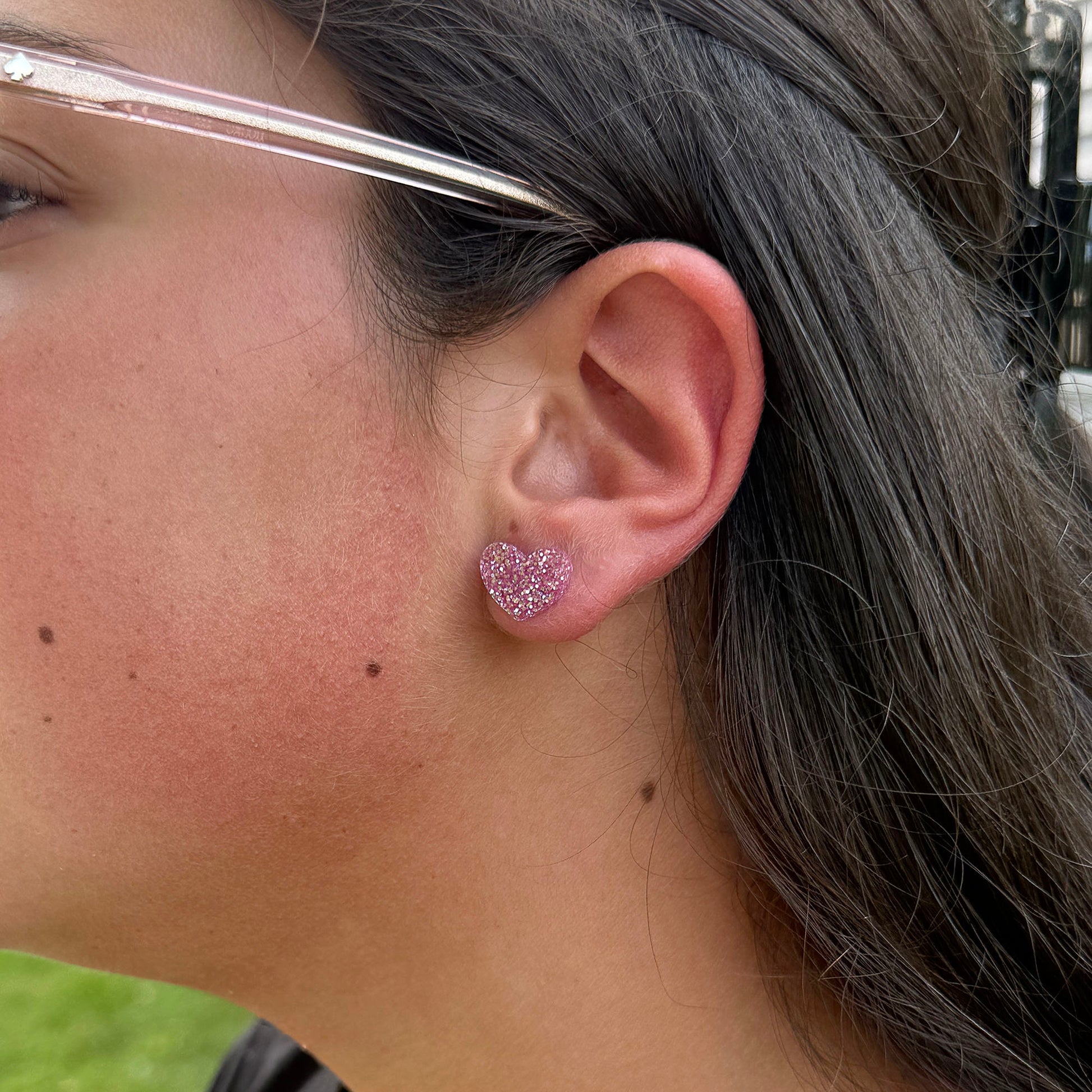 A close-up of a person's ear wearing a small glittery pink heart-shaped stud earring.