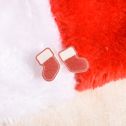 A pair of small Christmas stocking-shaped earrings with glittery red bodies and white cuffs, placed on an actual stocking