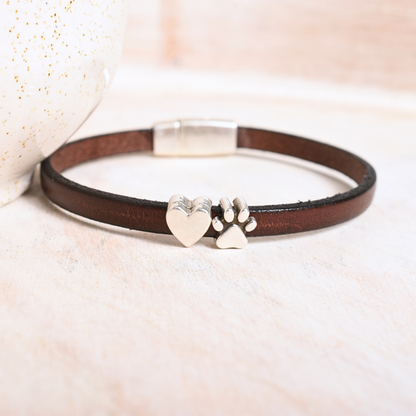 Brown leather bracelet with silver heart and paw print charm on a soft beige background