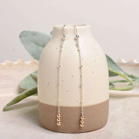 Ceramic vase with beaded earrings on a neutral background