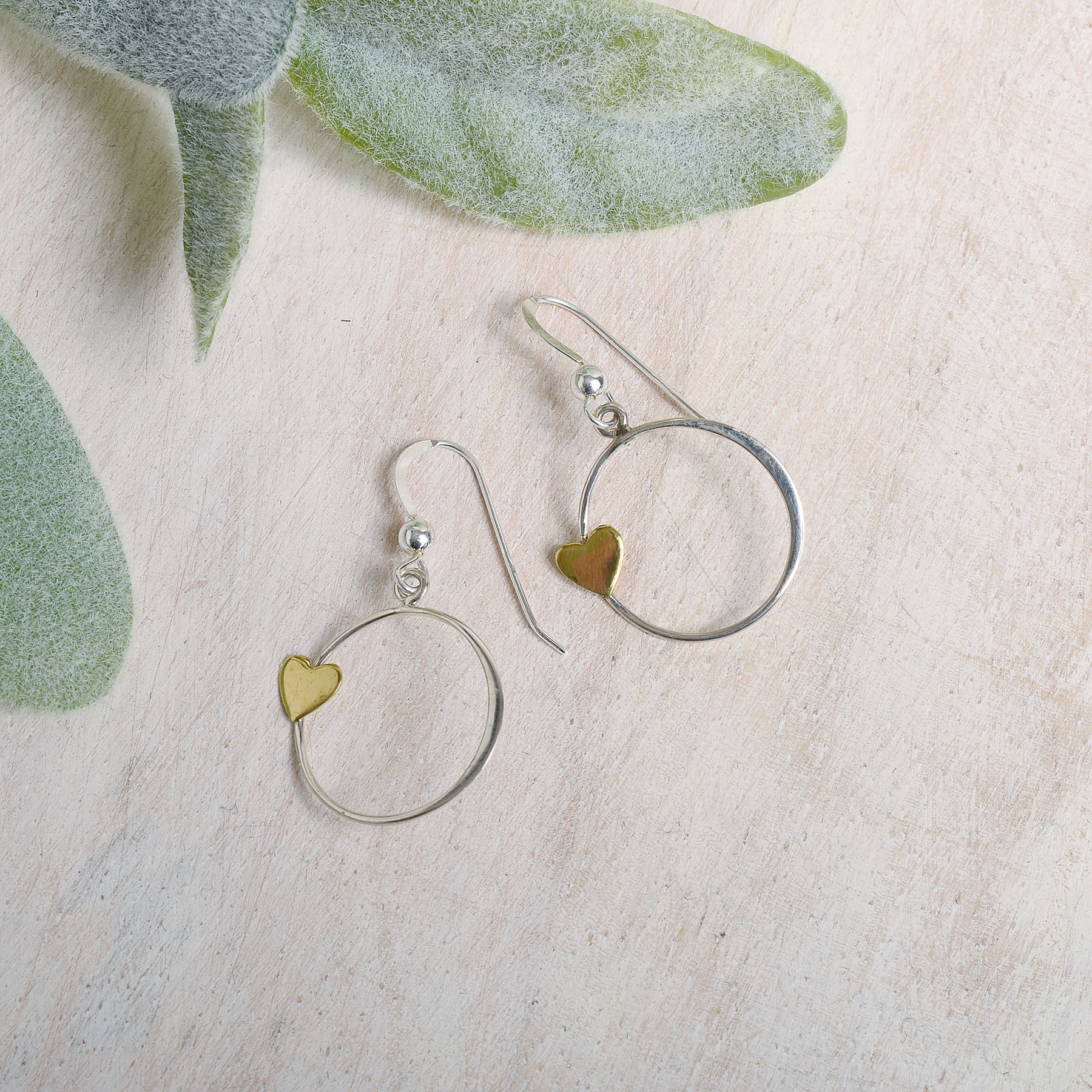 Silver earrings with bronze heart details on a light background