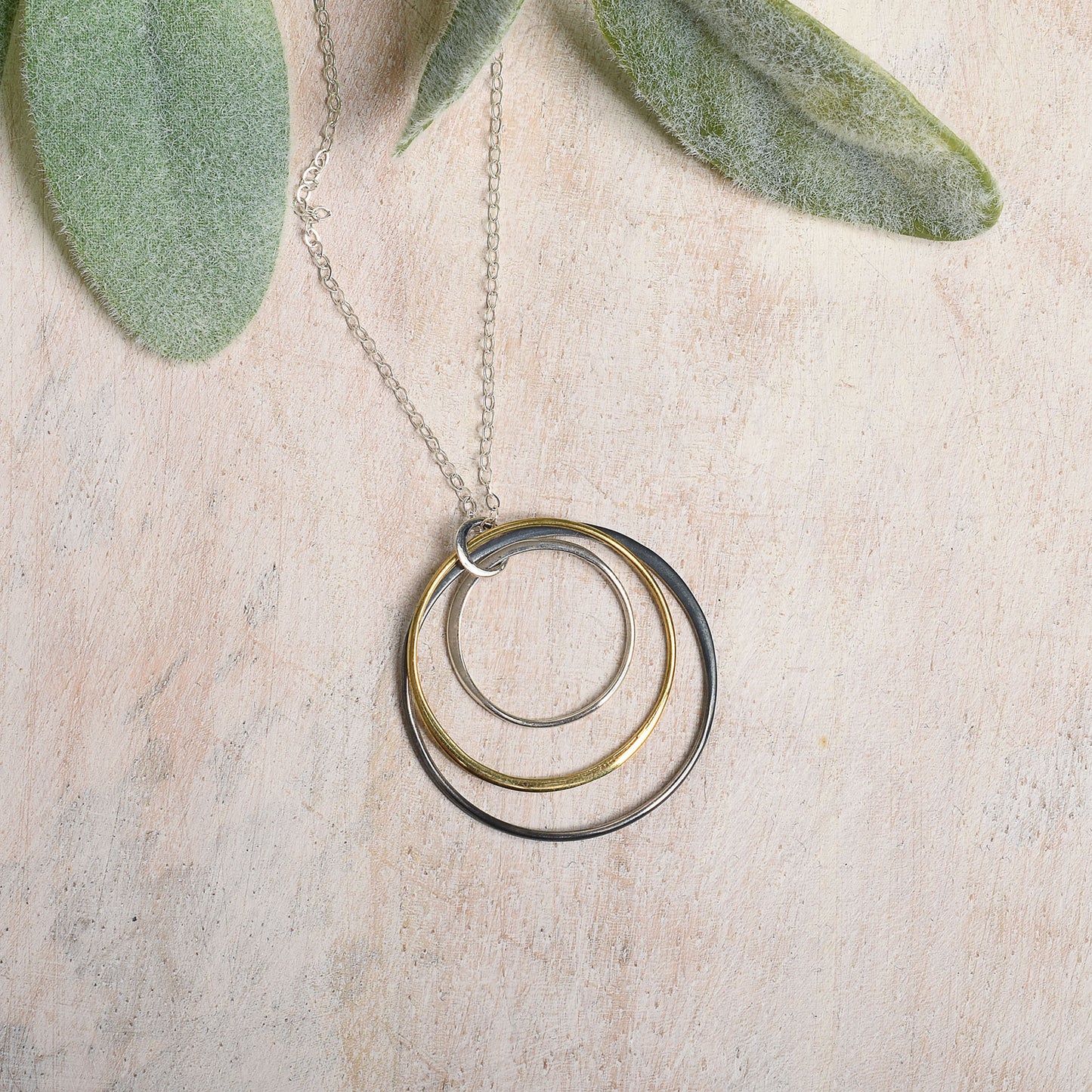 Necklace with three graduated rings on a light wooden surface with green leaves.