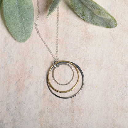 Necklace with three graduated rings on a light wooden surface with green leaves.
