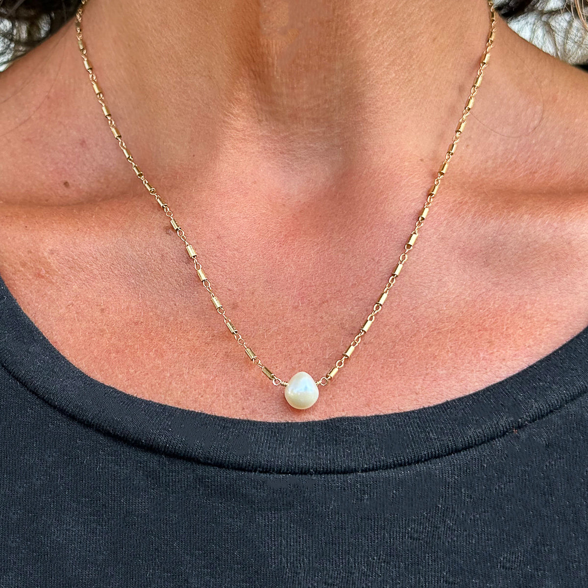 Teardrop pearl pendant on gold-filled chain modeled on a person's neck.