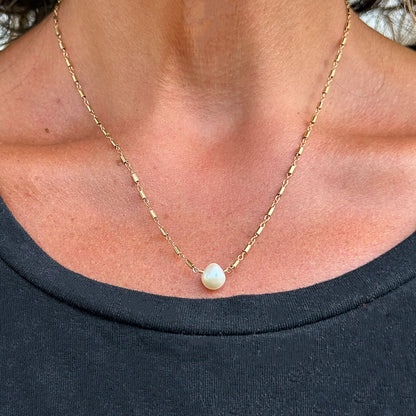 Teardrop pearl pendant on gold-filled chain modeled on a person's neck.