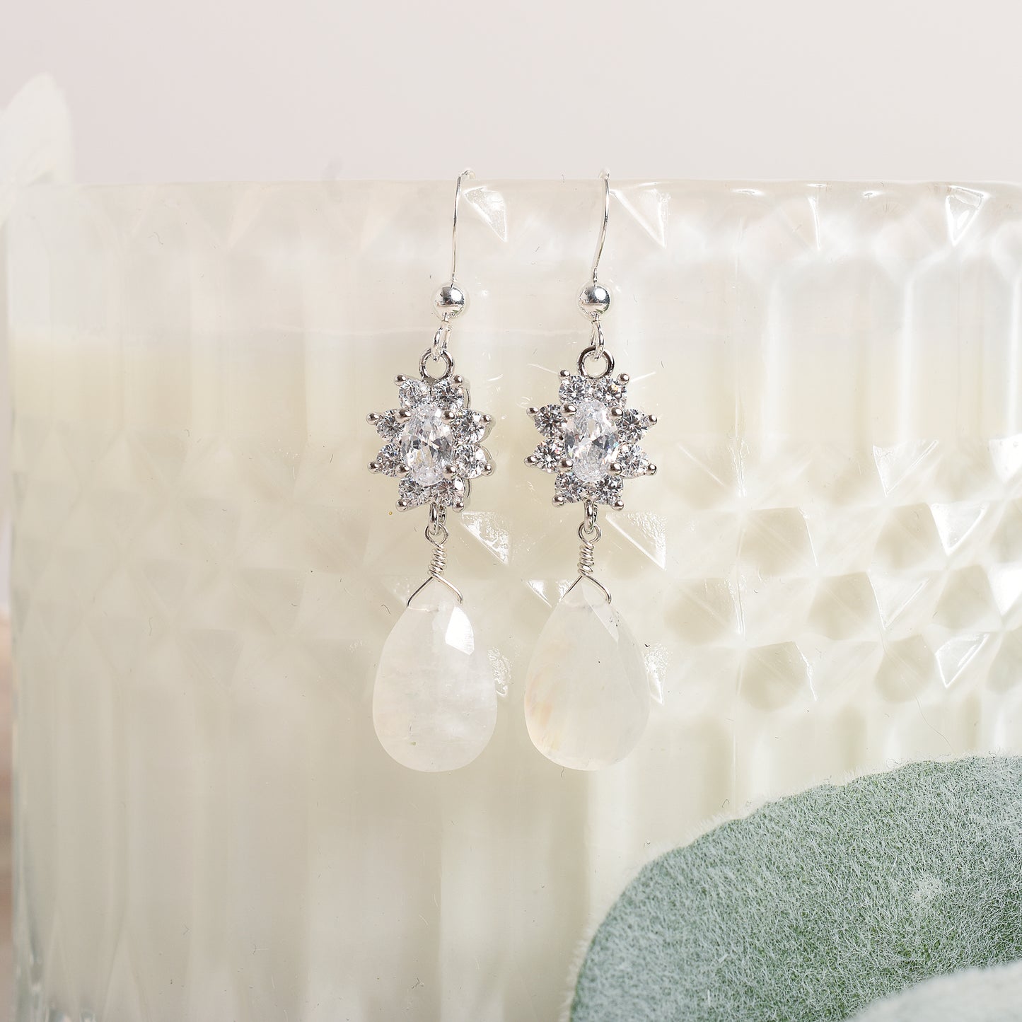 Silver earrings with clear stones and teardrop moonstone on a textured white surface.