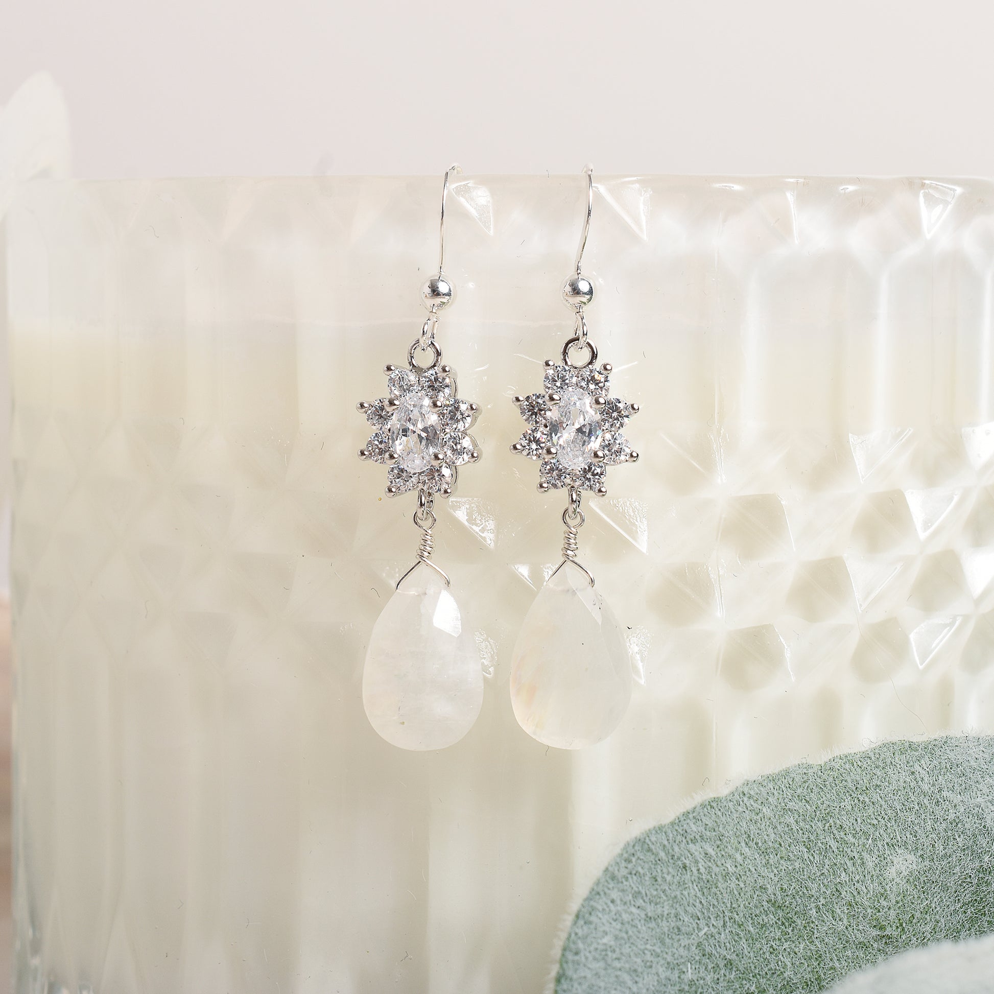 Silver earrings with clear stones and teardrop moonstone on a textured white surface.