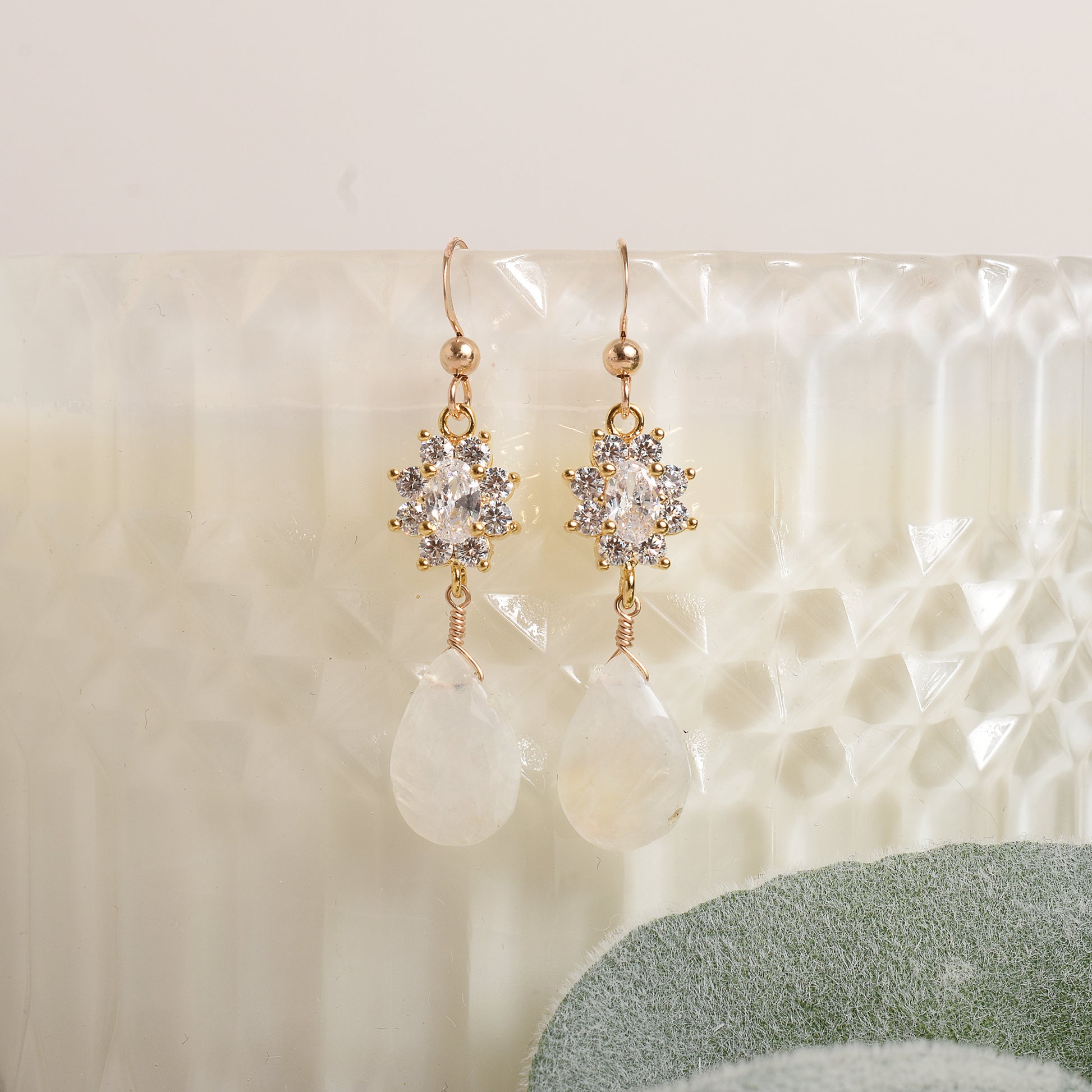 Pair of gold, crystal and moonstone earrings on a textured white surface