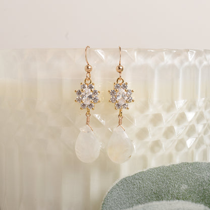 Pair of gold, crystal and moonstone earrings on a textured white surface