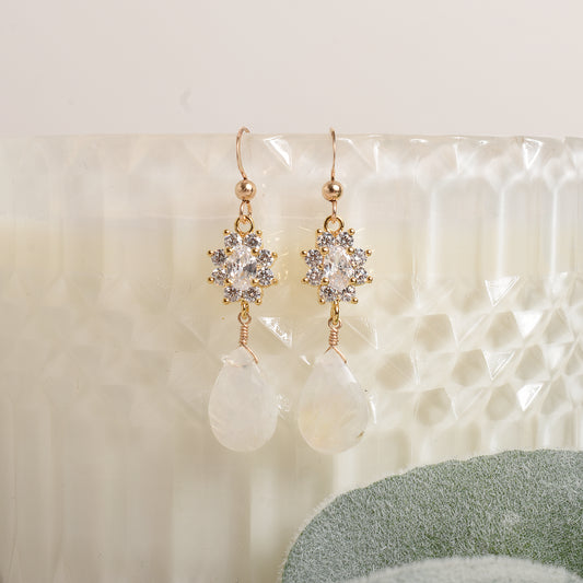 Pair of gold, crystal and moonstone earrings on a textured white surface