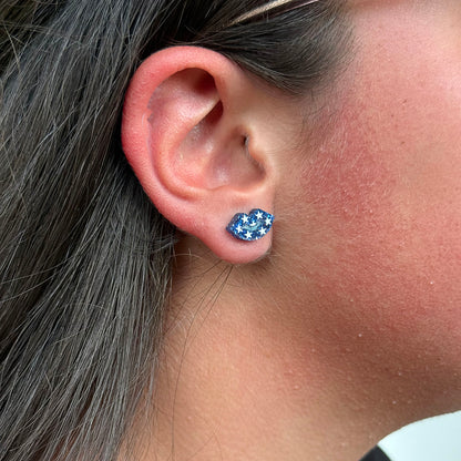 A close-up of a person's ear wearing a small stud earring with a blue background and white star pattern.