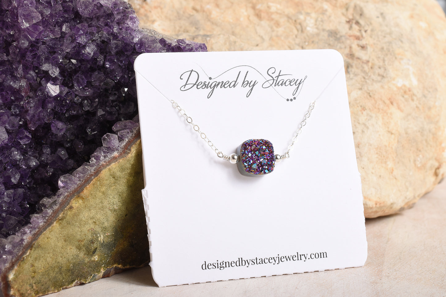 Necklace with a purple druzy stone on a display card against a stone background