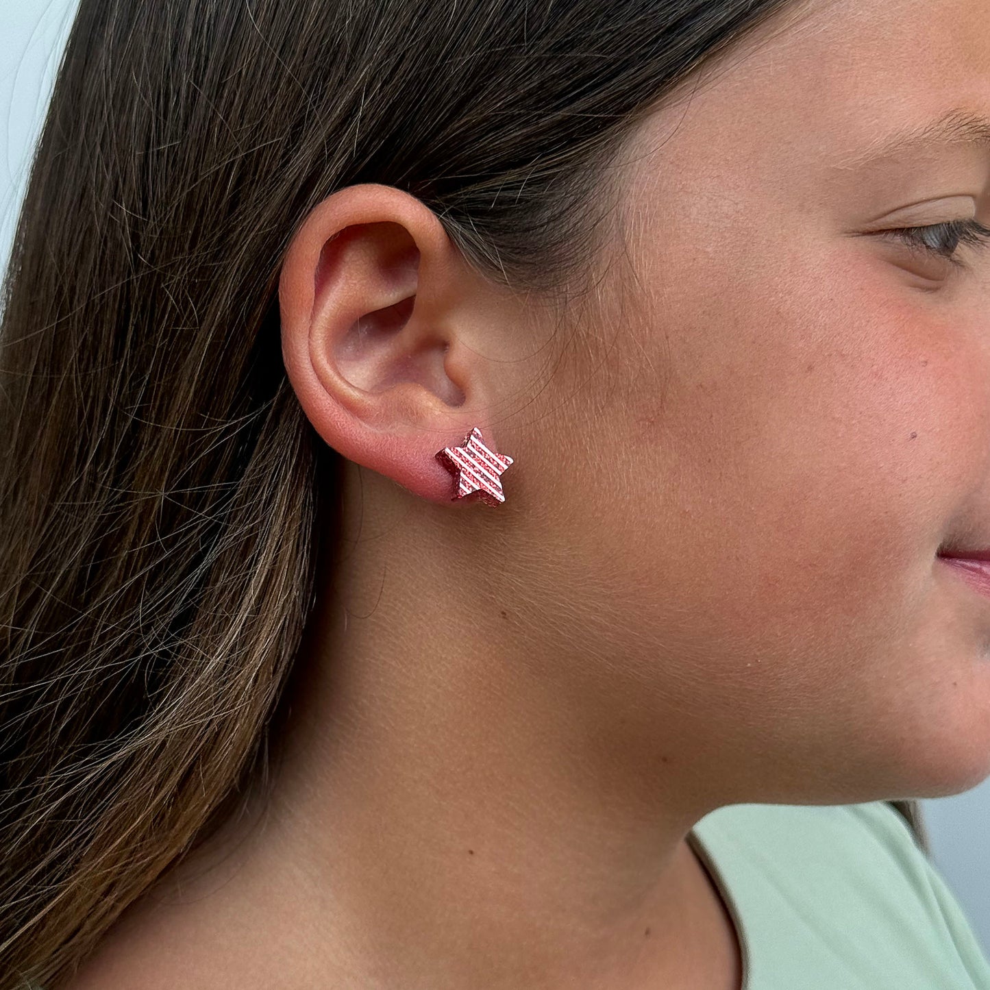 A close-up side profile of a girl wearing a small star-shaped stud earring with a red and white striped pattern.