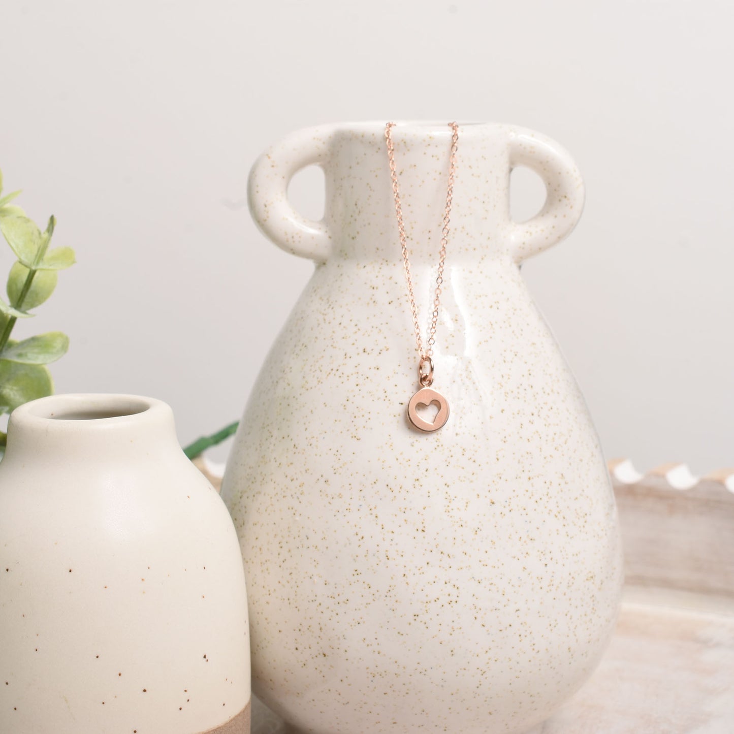 Necklace with a heart pendant draped over a ceramic vase on a light background