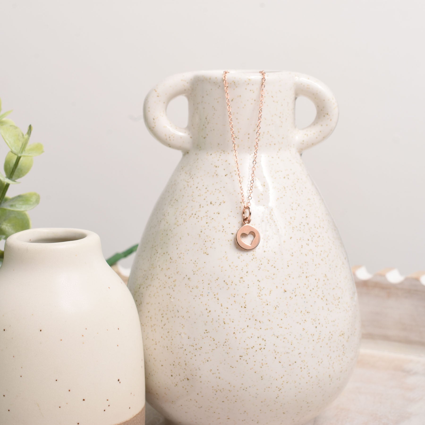 Necklace with a heart pendant draped over a ceramic vase on a light background